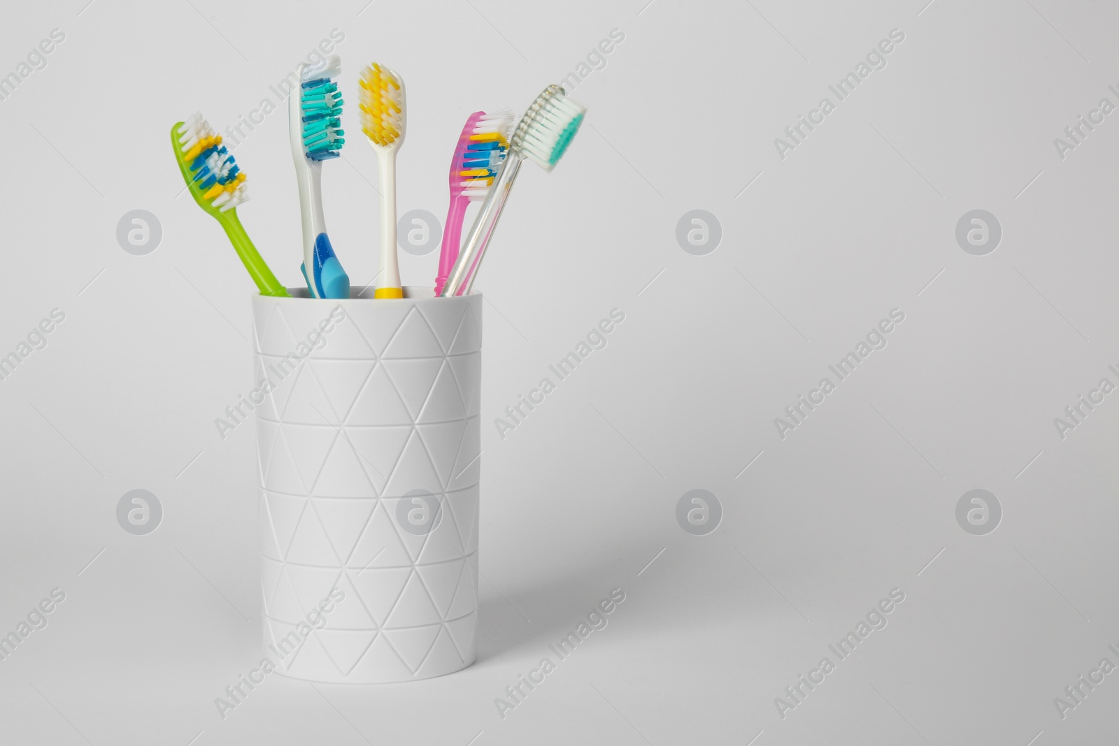 Photo of Different toothbrushes in holder on light grey background. Space for text