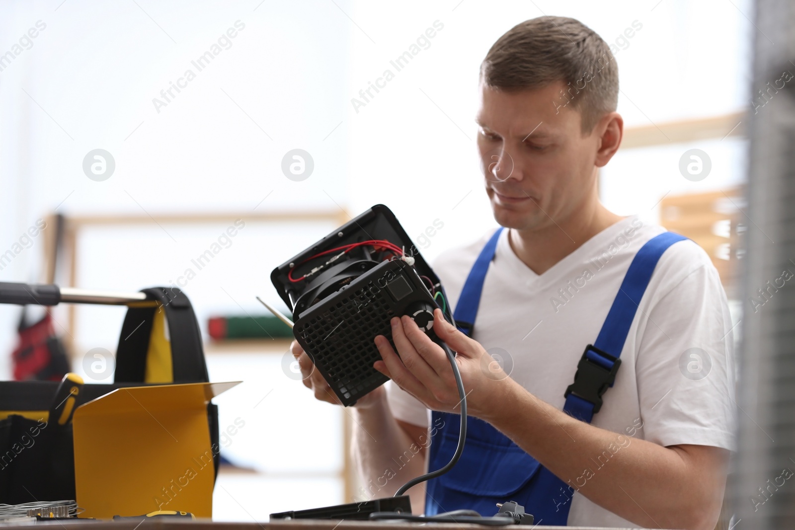 Photo of Professional technician repairing electric fan heater with screwdriver at table indoors