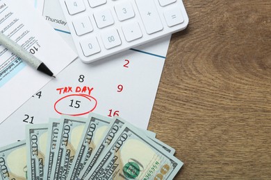 Calendar with date reminder about tax day, documents, pen, money and calculator on wooden table, flat lay. Space for text