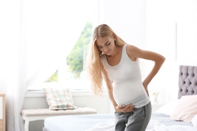 Photo of Young pregnant woman suffering from pain in bedroom. Gynecology concept