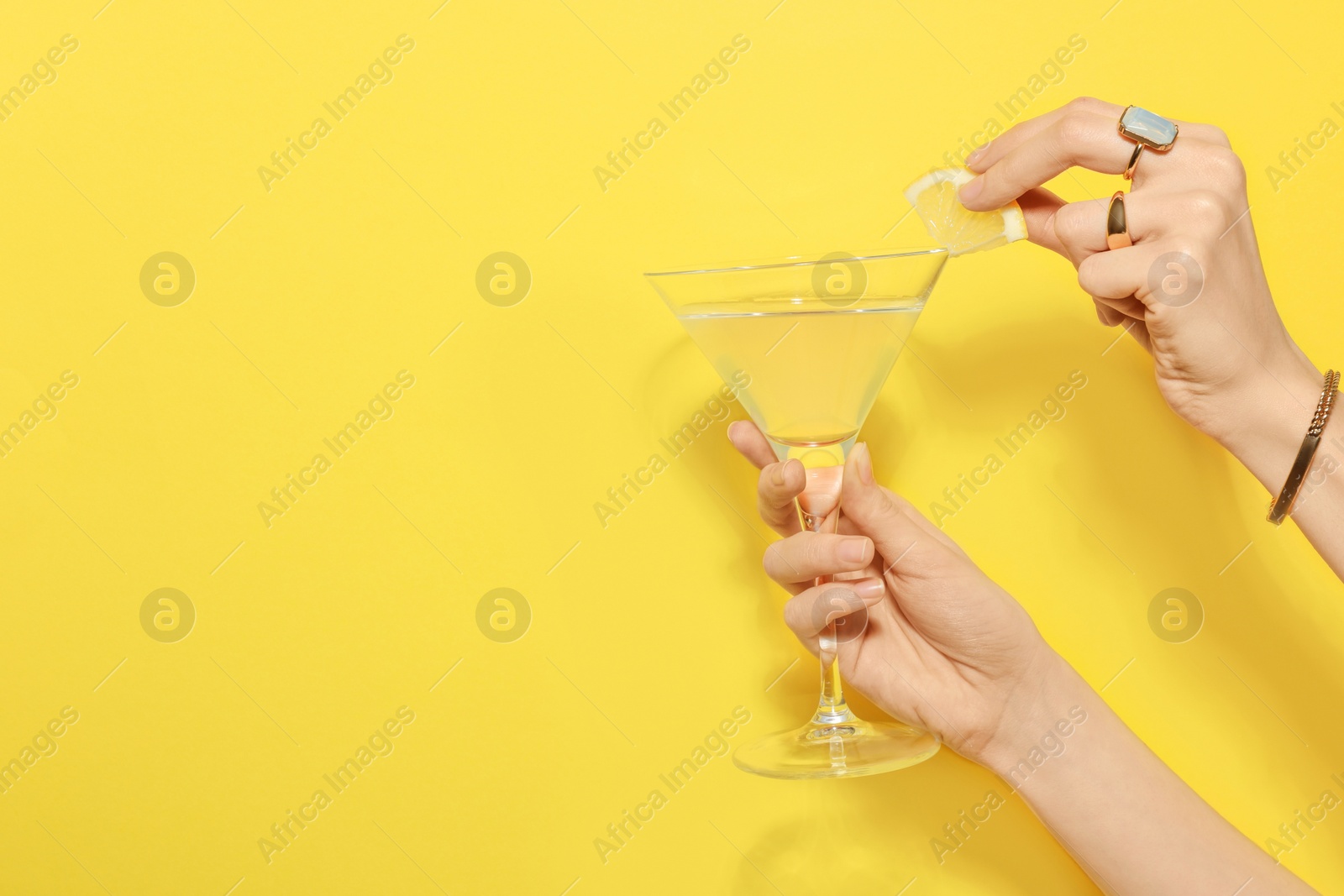 Photo of Woman adding lemon slice to martini glass of refreshing cocktail on yellow background, closeup. Space for text