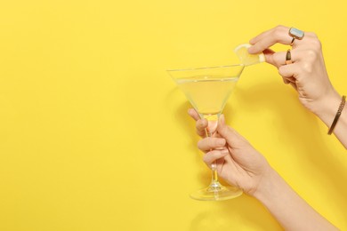 Photo of Woman adding lemon slice to martini glass of refreshing cocktail on yellow background, closeup. Space for text