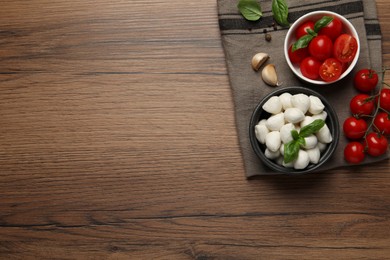 Delicious mozzarella balls, tomatoes and garlic on wooden table, flat lay. Space for text