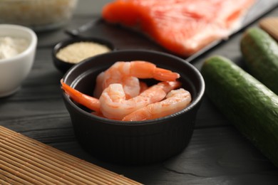 Photo of Fresh shrimps in bowl and other ingredients for sushi on black wooden table, closeup