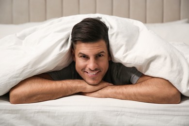Photo of Handsome man relaxing under soft blanket in bed at home
