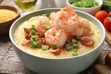 Photo of Fresh tasty shrimps, bacon, grits and green onion in bowl on wooden table, closeup