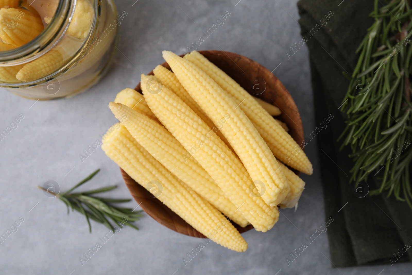 Photo of Tasty fresh yellow baby corns in bowl on grey table, top view