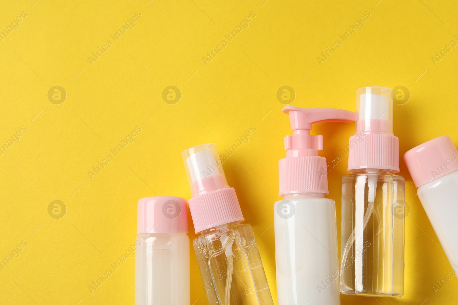 Photo of Cosmetic travel kit on yellow background, flat lay. Space for text