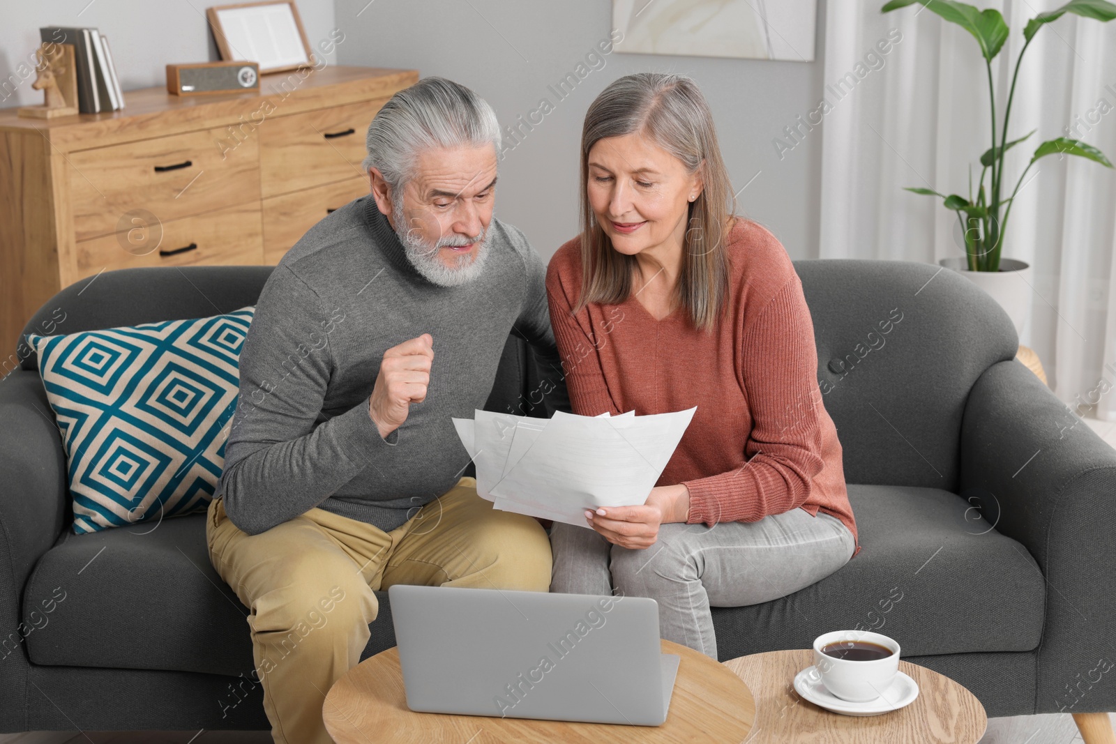 Photo of Elderly couple with papers and laptop discussing pension plan in room