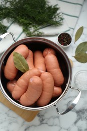Pan of delicious sausages, dill, bay leaf, pepper and salt on white marble table, flat lay