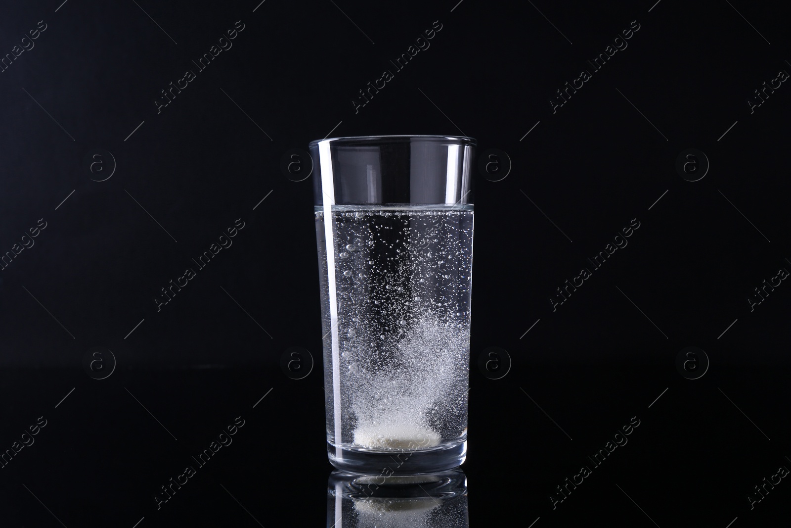 Photo of Effervescent pill dissolving in glass of water on black background