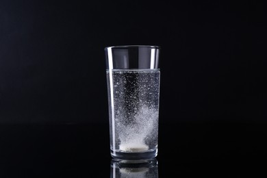 Photo of Effervescent pill dissolving in glass of water on black background