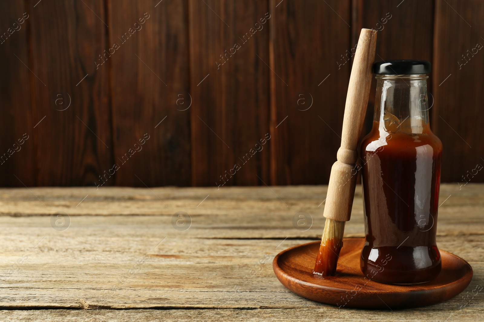 Photo of Tasty barbeque sauce in bottle and brush on wooden table. Space for text