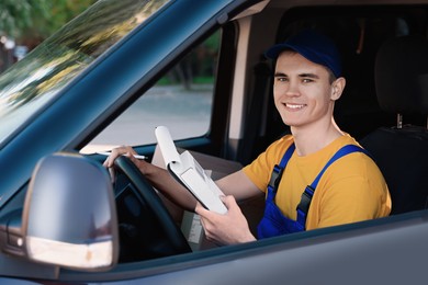 Courier with clipboard checking packages in car