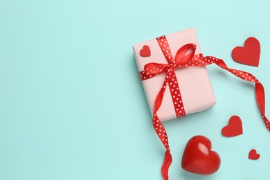 Photo of Gift box with decorative red hearts on turquoise background, flat lay. Space for text