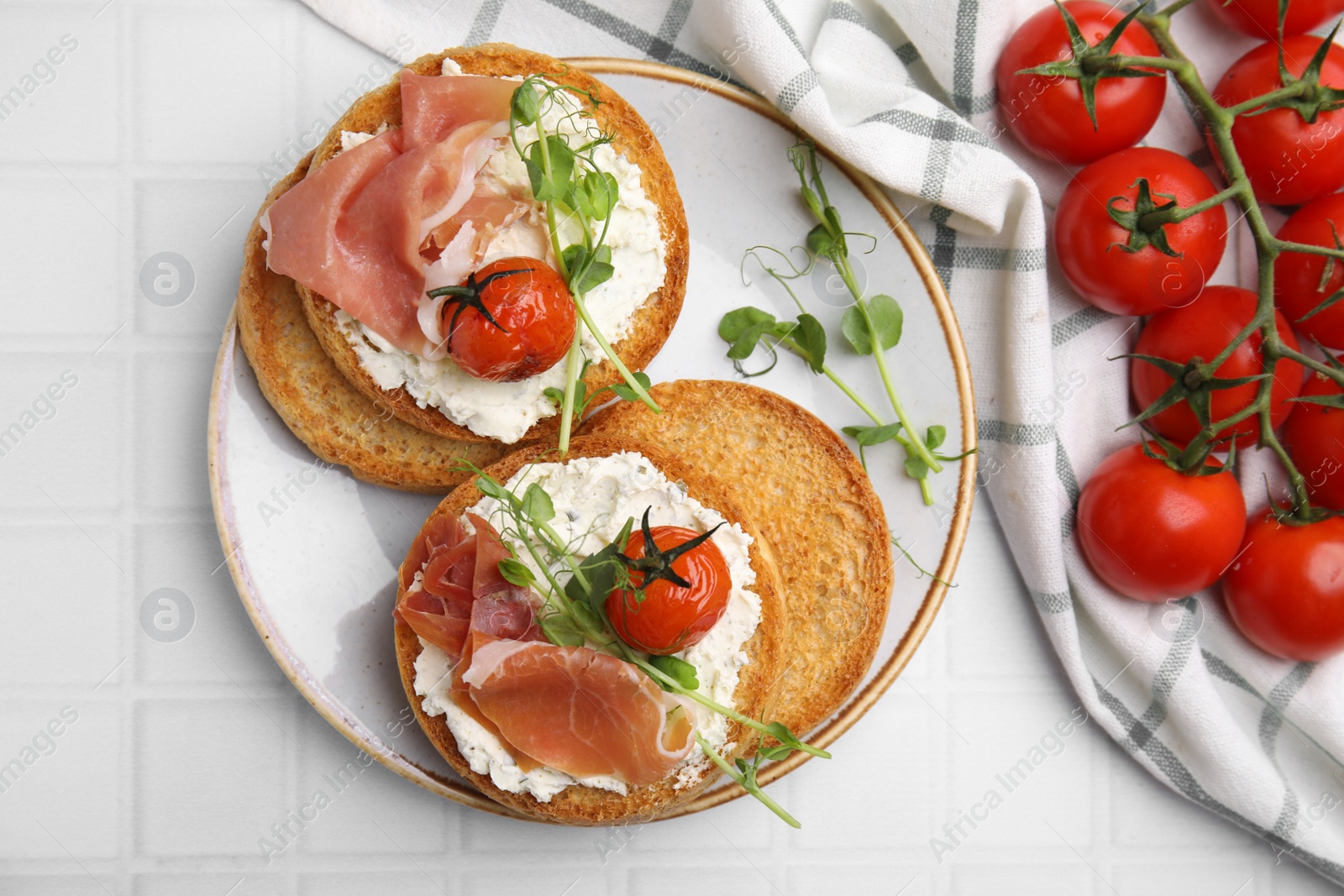 Photo of Tasty rusks with prosciutto, cream cheese and tomatoes on white table, flat lay