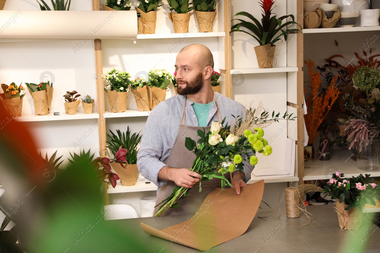 Photo of Florist making bouquet with fresh flowers at table in shop