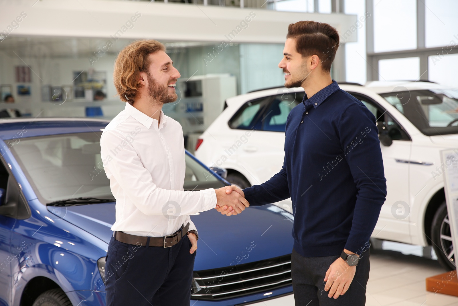 Photo of Salesman shaking hands with client in car dealership