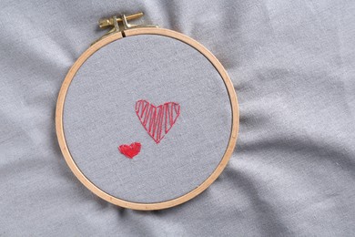 Embroidered red hearts on light grey cloth, top view