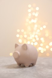 Photo of Piggy bank on grey table against blurred lights, space for text