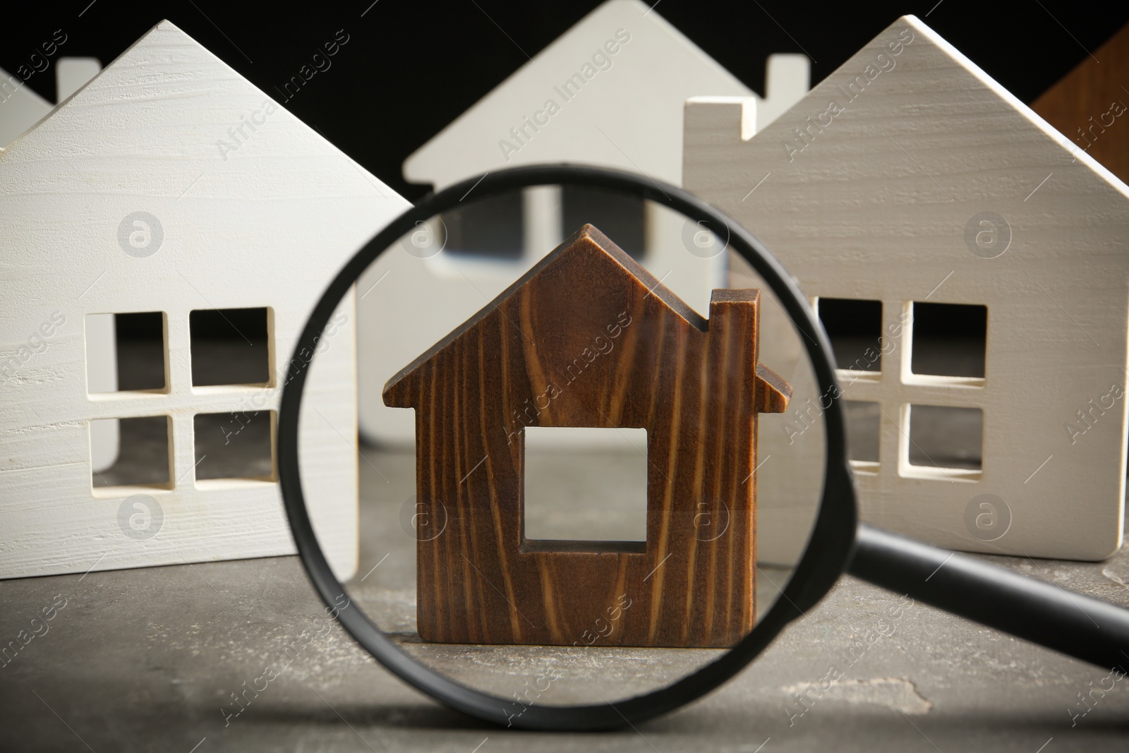 Photo of Magnifying glass and house models on grey stone table. Search concept