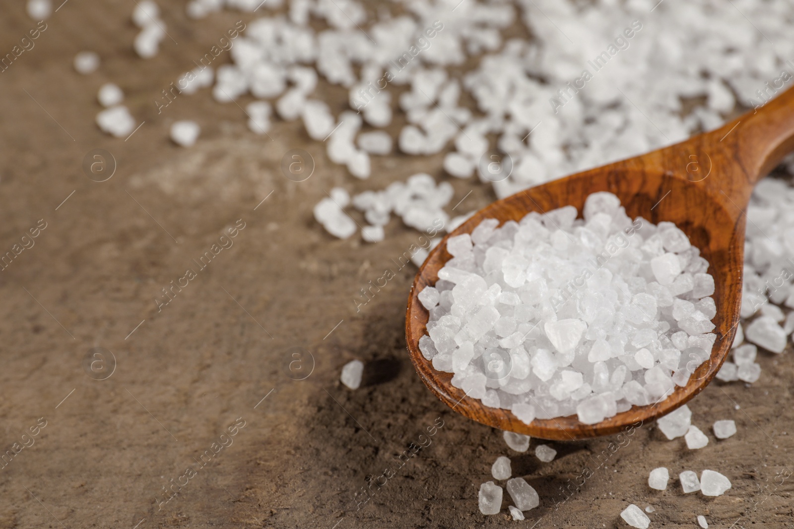 Photo of Spoon with natural sea salt on wooden table, closeup. Space for text