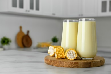 Photo of Tasty fresh corn milk in glasses and cobs on white table indoors. Space for text