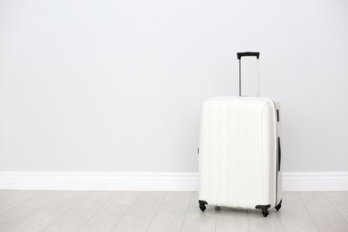 Photo of Modern suitcase on floor near light wall. Space for text