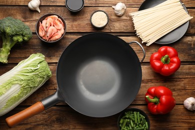 Photo of Empty iron wok and raw ingredients on wooden table, flat lay
