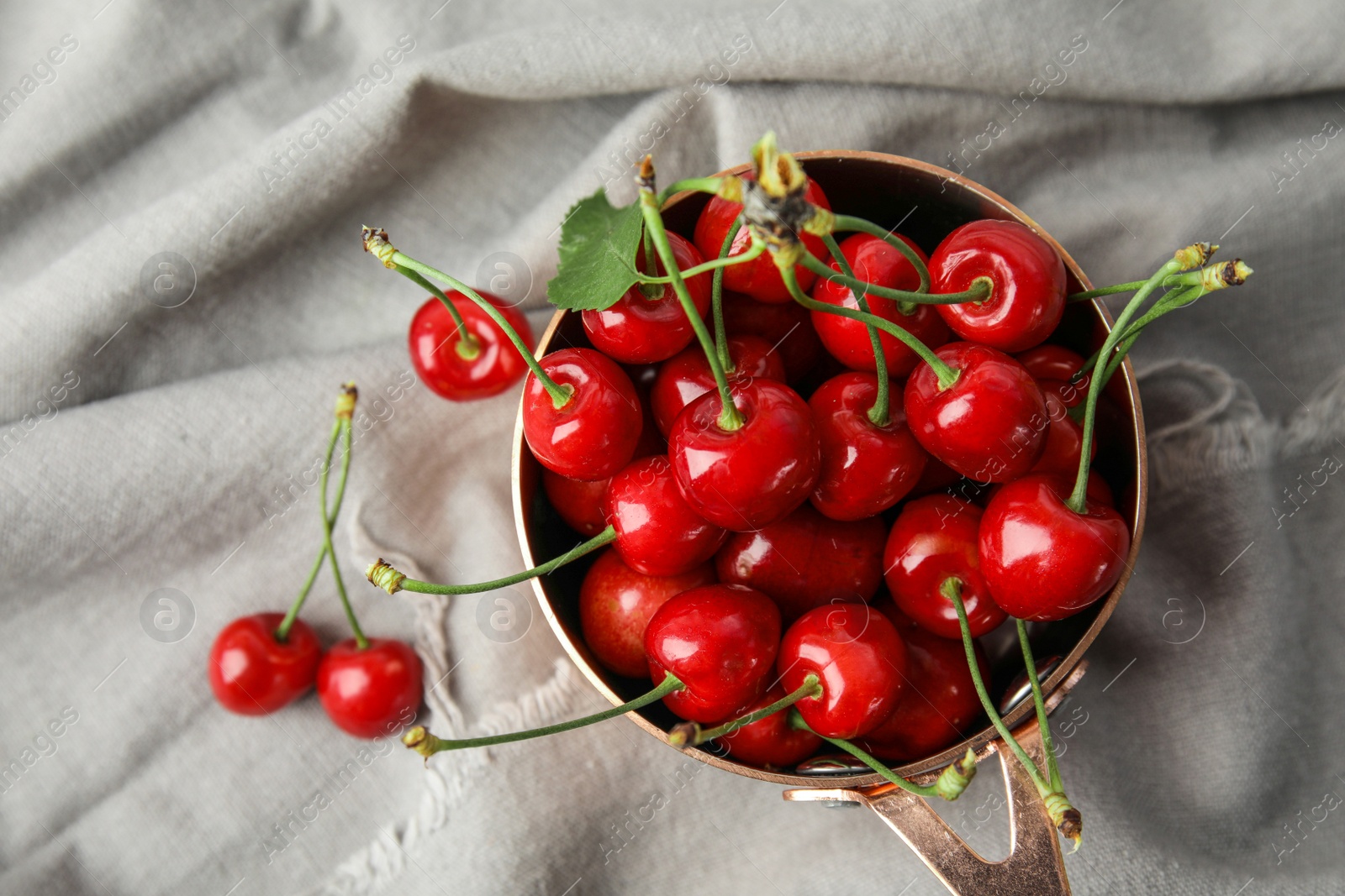 Photo of Saucepan with sweet red cherries on fabric, top view