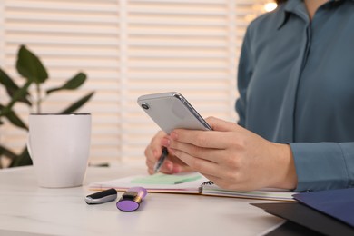 Photo of Woman taking notes while using smartphone at white marble table indoors, closeup