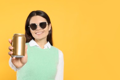 Beautiful happy woman holding beverage can on yellow background. Space for text