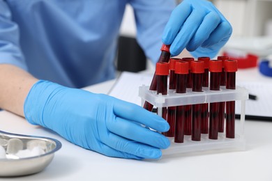 Laboratory testing. Doctor with blood samples in tubes at white table indoors, closeup