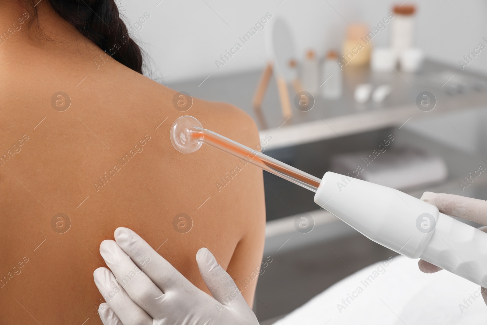 Photo of Woman undergoing physiotherapy procedure with darsonval in salon, back view