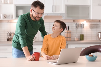 Little boy and his dad using laptop in kitchen