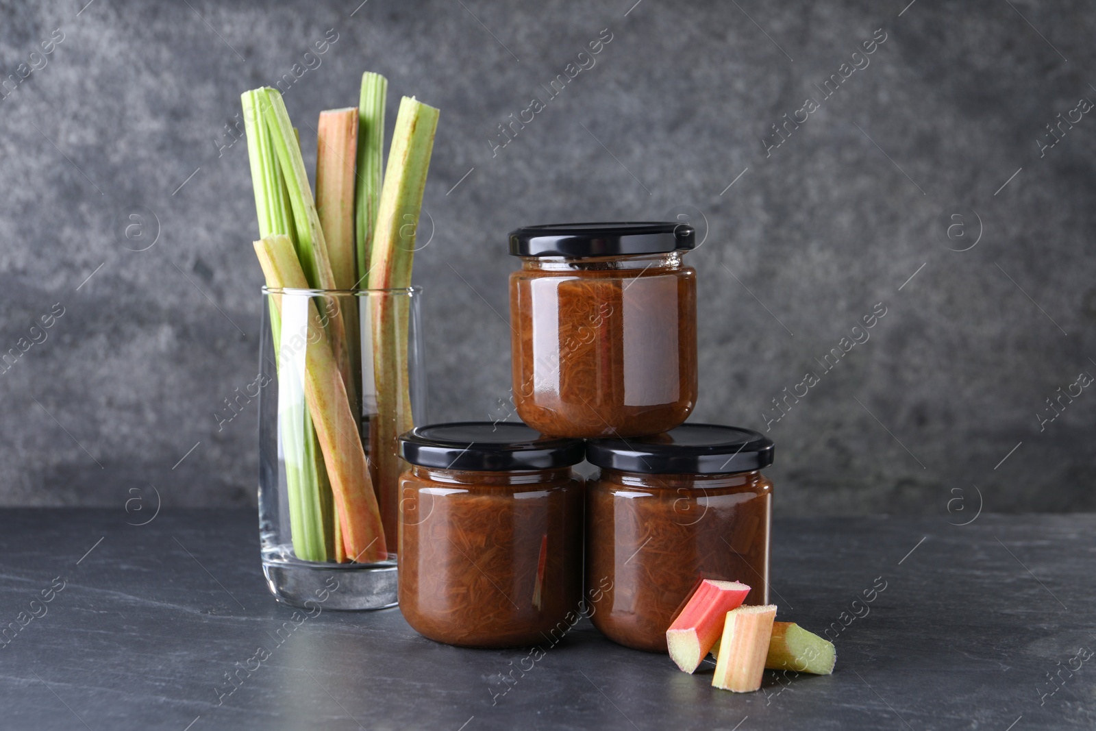 Photo of Jars of tasty rhubarb jam and stalks on grey table