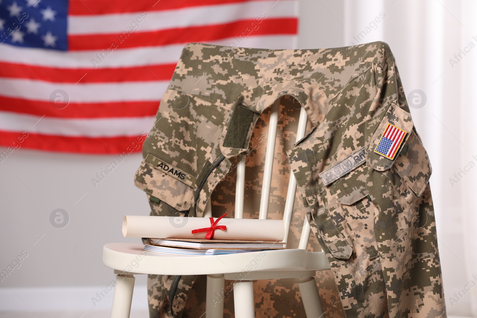 Photo of Chair with soldier uniform, notebooks and diploma near flag of United States indoors. Military education