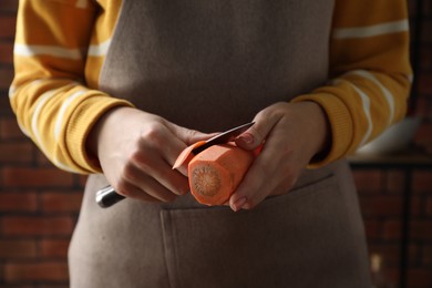 Photo of Woman peeling fresh carrot with knife indoors, closeup