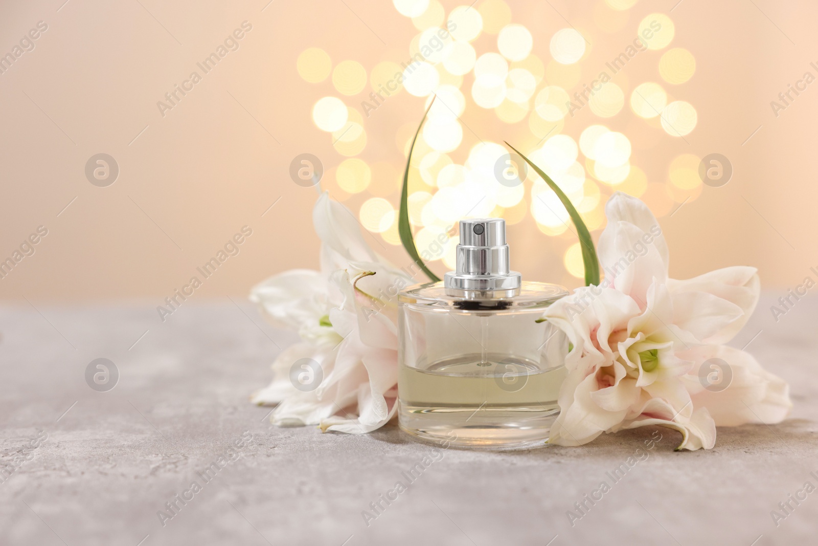 Photo of Bottle of perfume and beautiful lily flowers on table against beige background with blurred lights, space for text