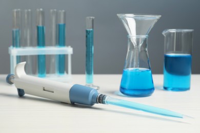 Laboratory analysis. Micropipette and different glassware with liquids on white wooden table, closeup