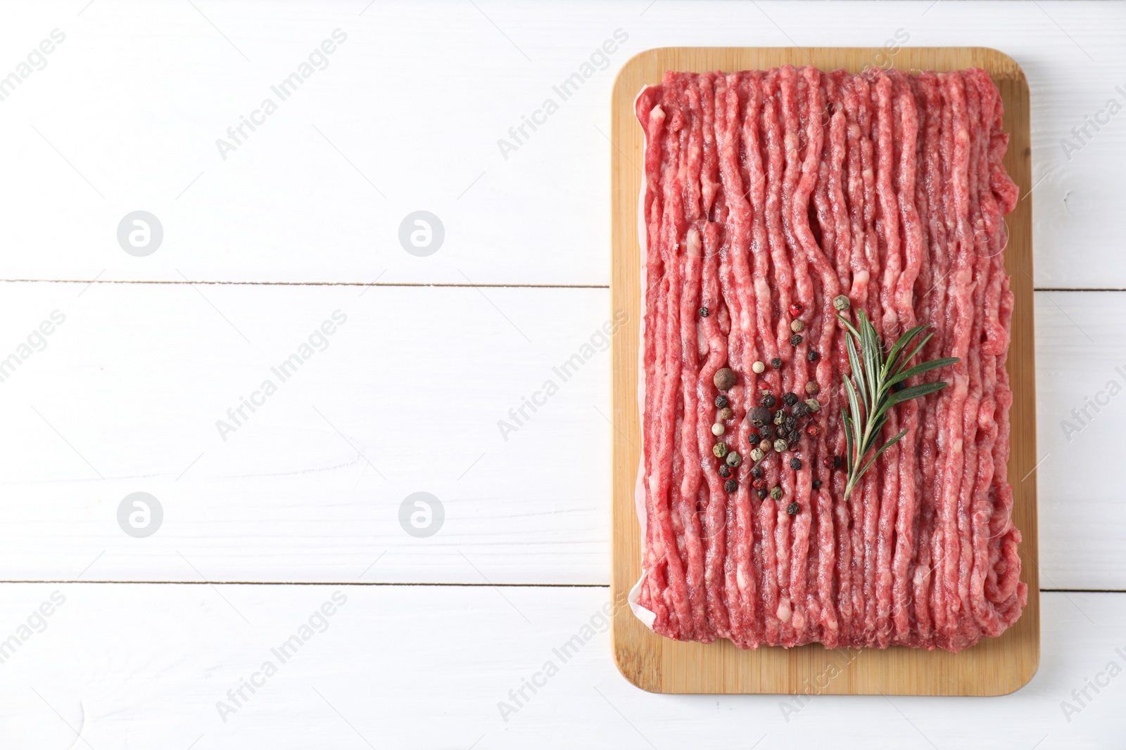 Photo of Raw ground meat, rosemary and peppercorns on white wooden table, top view. Space for text