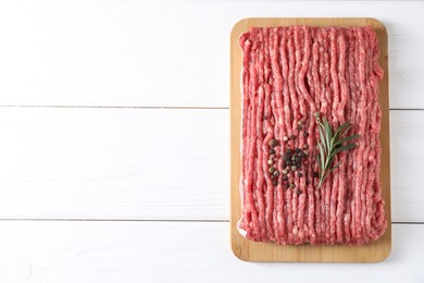 Photo of Raw ground meat, rosemary and peppercorns on white wooden table, top view. Space for text