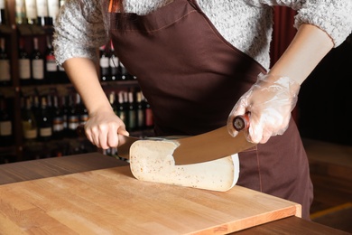 Photo of Seller cutting delicious cheese on table in store