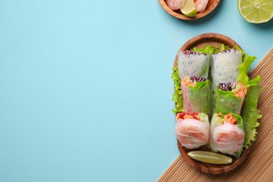 Photo of Delicious spring rolls with shrimps and lime on light blue background, flat lay. Space for text