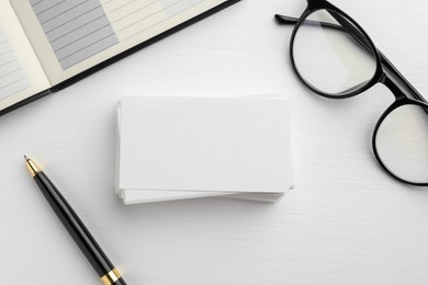 Blank business cards, glasses, notebook and pen on white table, flat lay. Mockup for design