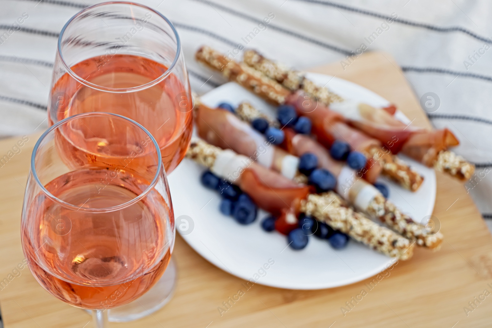 Photo of Glasses of delicious rose wine and food on white picnic blanket, closeup