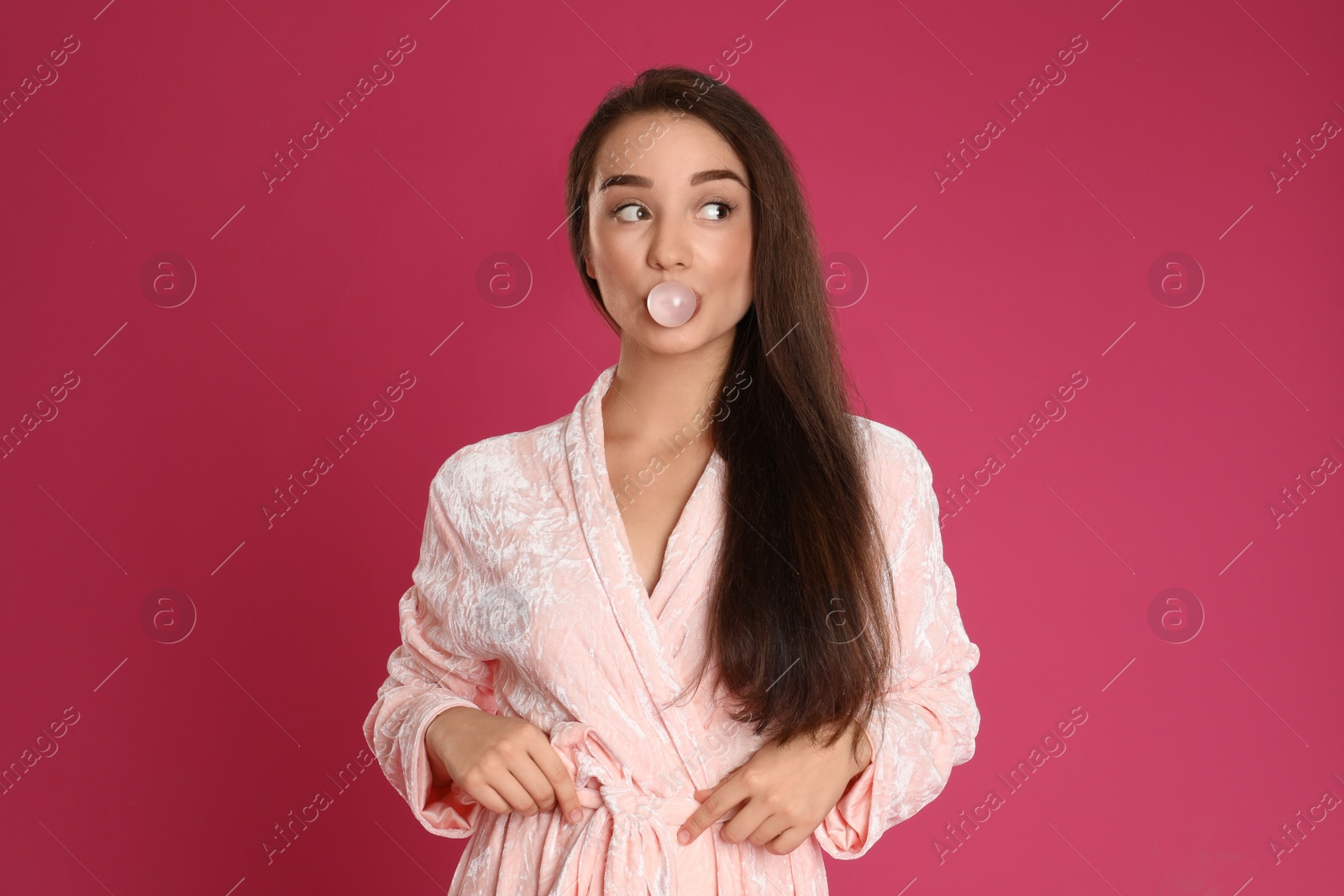 Photo of Young woman in bathrobe blowing chewing gum on crimson background