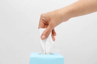 Photo of Woman taking paper tissue from box on light background, closeup