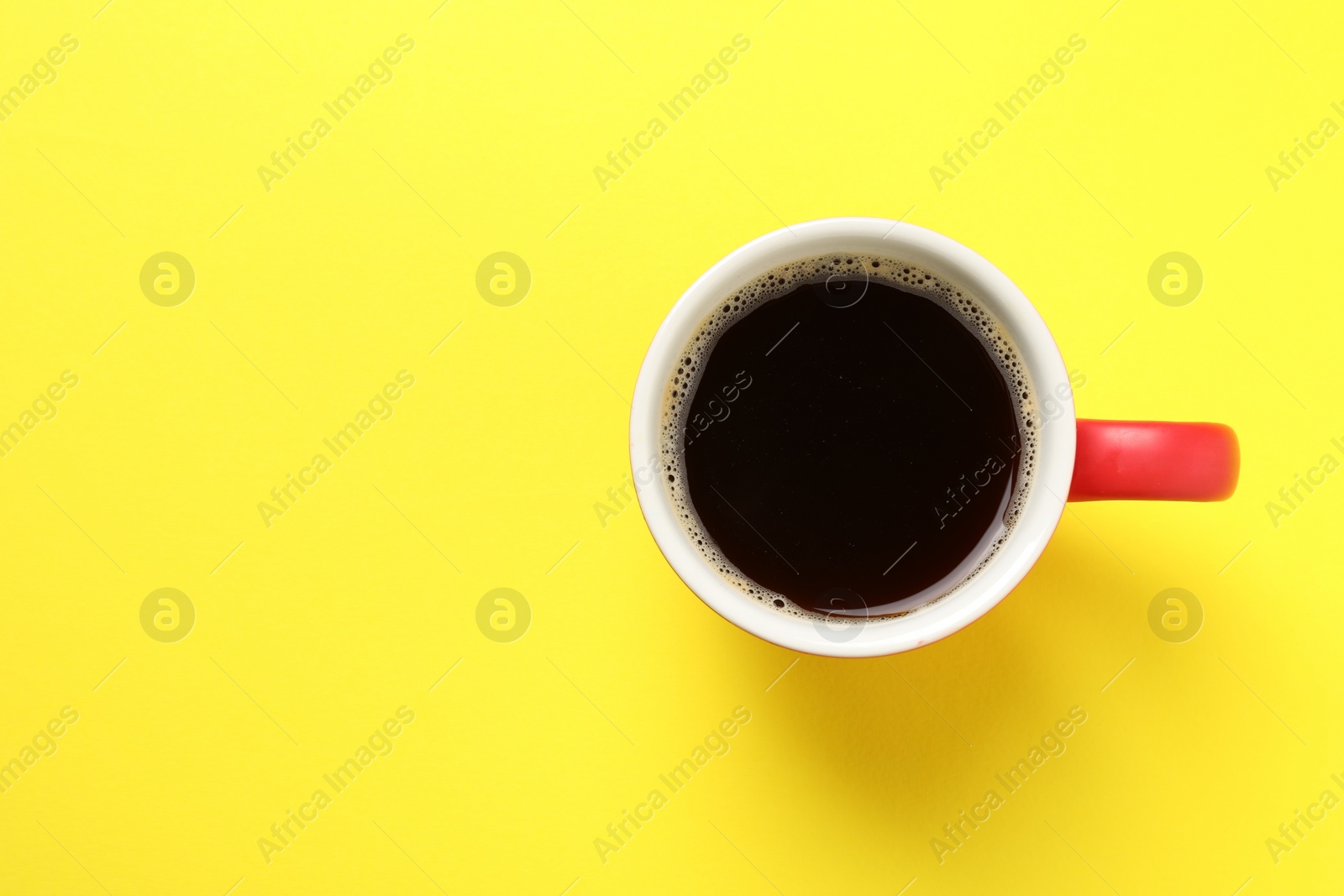 Photo of Aromatic coffee in cup on yellow background, top view. Space for text