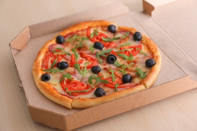 Photo of Cardboard box with tasty pizza on wooden table
